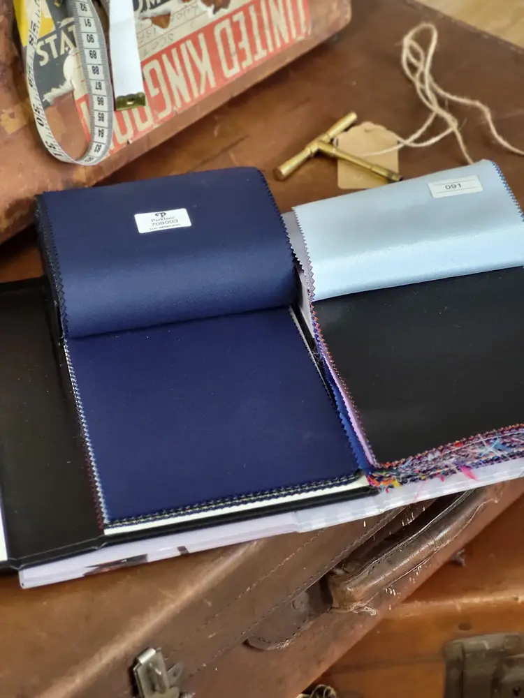 Open fabric swatch books showing navy merino wool and pale blue shirting on a vintage leather case